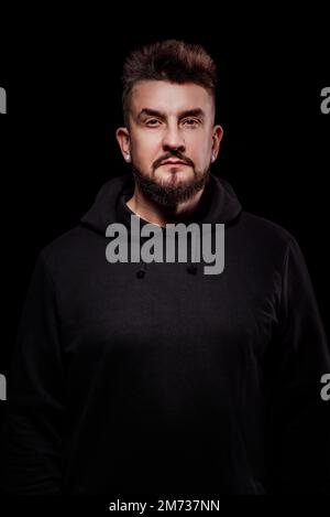 portrait d'un homme dans le studio sur fond noir ; couché dans une veste noire avec capuche ; capuche sur la tête Banque D'Images