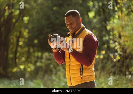 Gros plan un photographe afro-américain prenant des photos avec un appareil photo sur le parc vert de la ville - activité de loisirs, diversité et concept de passe-temps Banque D'Images