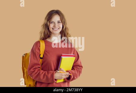 Portrait d'une jeune fille étudiante souriante avec sac à dos et dossiers sur fond beige. Banque D'Images