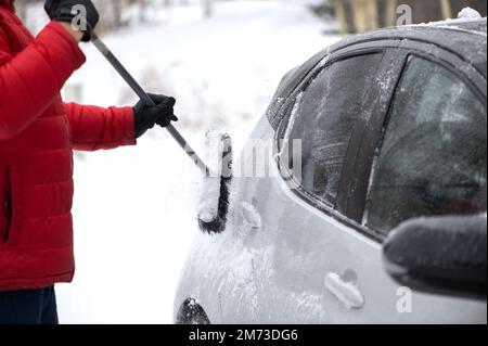 L'homme nettoie la voiture de la neige avec une brosse. Concept de mauvais temps de neige. Banque D'Images