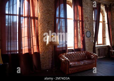 Fenêtres dans la salle de bibliothèque vide avec un mur de briques. Canapé en cuir de style vintage. Le mobilier dans la chambre. Intérieur brun foncé. Banque D'Images