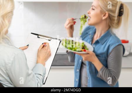 Une nutritionniste souriante conseille une jeune femme sur la nutrition et le régime appropriés. Le médecin montre un schéma de perte de poids sans un mauvais effet sur Banque D'Images