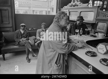 Londres. Fin 1960s. Un groupe d'amis qui se socialisent au pub Duke of Wellington, situé à l'angle de Portobello Road et Elgin Crescent, dans le quartier de Notting Hill du Royal Borough de Kensington et Chelsea, dans l'ouest de Londres. Une dame âgée portant un manteau et un filet à cheveux est debout au bar, attendant d'être servie. Banque D'Images