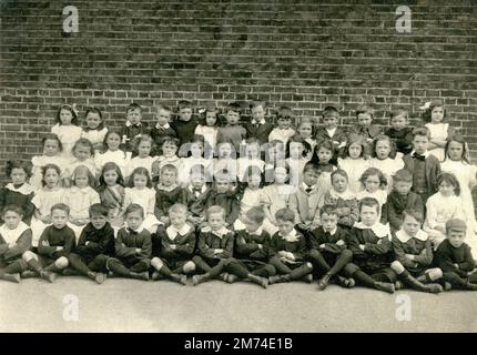 Londres. vers. 1908. Une classe d'enfants en bas âge pose pour une photographie de groupe devant leur bâtiment scolaire. Les jeunes filles et les jeunes garçons fréquentent l'école de la rue Gopsall, Hackney. Beaucoup de filles portent des pinafores et certains des garçons ont des colliers de style 'Peter Pan' en lin raides ou en dentelle. Banque D'Images