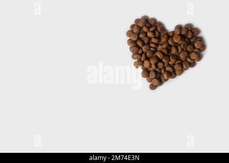 Séchez les aliments pour animaux de compagnie en forme de cœur isolé sur un fond blanc, espace de copie. Aliments diététiques en granulés pour chats et chiens. Nourriture préférée pour animaux. Prise Banque D'Images
