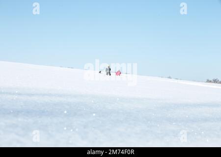 Deux silhouettes d'enfants en combinaison bleue et rouge contre un ciel bleu clair. Les gens à l'horizon. Les enfants ont pris la distance sur la route Banque D'Images