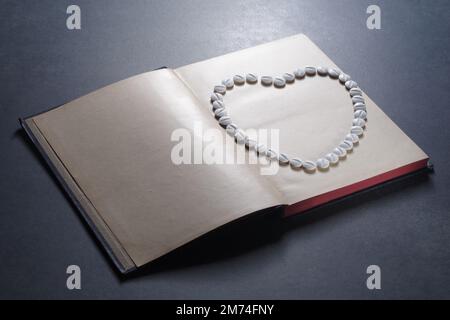 Symbole de coeur disposé à partir de pilules sur un livre. Droit en médecine. Concept de droit médical et de crimes médicaux Banque D'Images