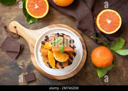 Fêtez la fête du Pancake, petit déjeuner américain sain. Délicieuses crêpes aux bananes avec chocolat et oranges rouges sur table rustique. Vue de dessus. Banque D'Images