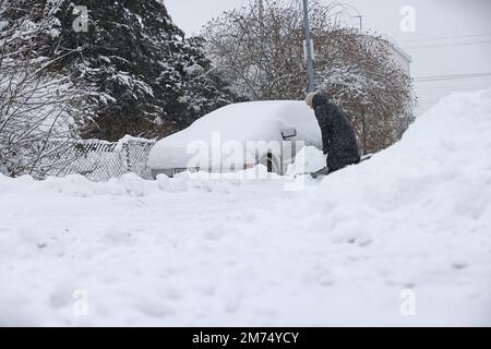 Météo saisonnière, fortes chutes de neige à Motala, en Suède, vendredi après-midi. Une femme pelle la neige d'une voiture enneigée. Banque D'Images