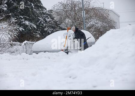 Météo saisonnière, fortes chutes de neige à Motala, en Suède, vendredi après-midi. Une femme pelle la neige d'une voiture enneigée. Banque D'Images