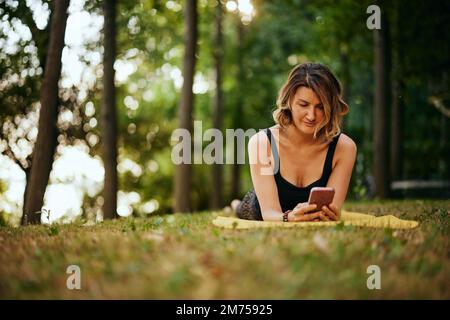 Une femme yogi est couché sur le ventre en forêt et utilise le téléphone. Banque D'Images