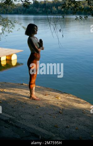 Une femme yogi fait la salutation au soleil près de l'eau sur un quai au coucher du soleil. Banque D'Images