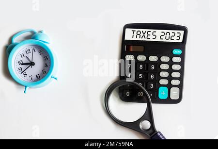 Calculatrice avec le texte TAXS 2023 repose sur un fond blanc avec une horloge et une loupe. Concept commercial et financier Banque D'Images