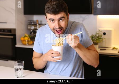 Un adorable gars mangeant des nouilles instantanées dans la cuisine Banque D'Images