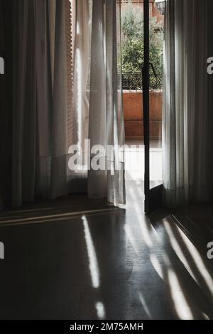 Intérieur de la chambre avec portes-fenêtres en verre donnant sur le balcon. Rideaux soufflant et se déplaçant vers l'intérieur dans la pièce. Image à contraste élevé. Concept de voyage phot Banque D'Images