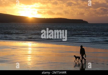 Ayr, Ayrshire, Écosse. UK Jan 2023 .Une figure silhouettée e avec le chien aime une promenade en soirée le long de la plage à Ayr comme l'espace de couchers de soleil pour la copie ou le texte. Image romantique de style de vie Banque D'Images