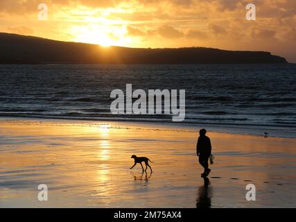 Ayr, Ayrshire, Écosse. UK Jan 2023 .Une figure silhouettée e avec le chien aime une promenade en soirée le long de la plage à Ayr comme l'espace de couchers de soleil pour la copie ou le texte. Image romantique de style de vie Banque D'Images