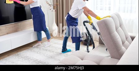 Les nettoyeurs professionnels en uniforme bleu lave-de-chaussée et d'essuyer la poussière sur les meubles dans la salle de séjour de l'appartement. Le concept de service de nettoyage Banque D'Images