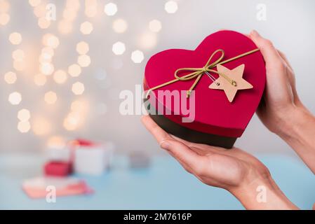 St. Cadeaux de la Saint-Valentin dans une boîte en forme de coeur dans les mains. Espace de copie pour message d'amour. Choisissez le cadeau de nouvel an pour la personne aimée, gros plan, bokeh Banque D'Images