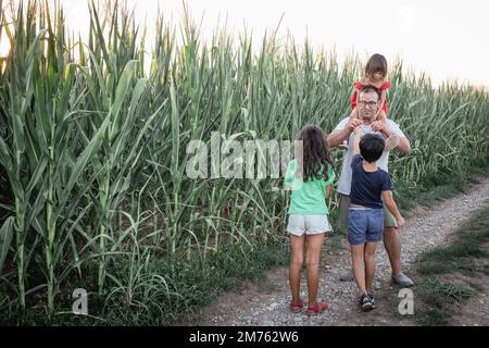 les filles plus âgées parlent à leur père et à leur petite sœur assis sur son cou sur la route de campagne Banque D'Images