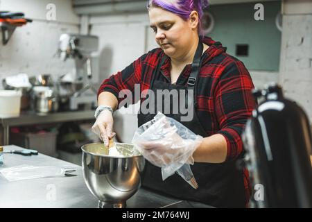 Personne remplissant sac de pâtisserie jetable avec glaçage à la crème de beurre pour décorer cupcakes et tartes. Chef féminin professionnel dans la cuisine. Photo de haute qualité Banque D'Images