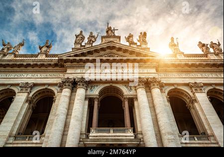 Basilica di San Giovanni in Laterano (Archibasilique papale de St John Lateran), Rome, Italie. Vue avant de la façade, des statues, du ciel et du soleil. Concept de soupir Banque D'Images