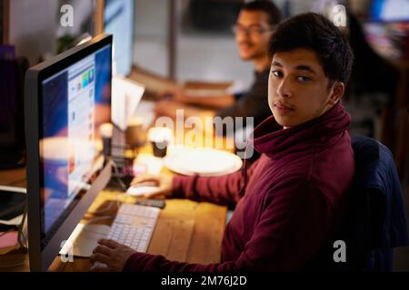 Getting the job done. a group of young coworkers working in a dimly-lit office. Stock Photo