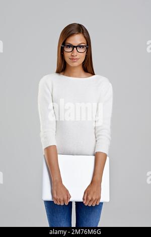 J'ai du travail à faire. Photo en studio d'une jeune femme attrayante tenant un ordinateur portable sur fond gris. Banque D'Images