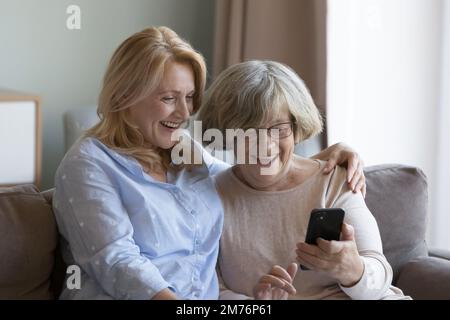 Une fille mûre joyeuse et une mère âgée partageant un téléphone portable Banque D'Images