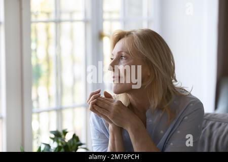 Une femme blonde d'âge moyen, bien réfléchie et positive, assise sur un canapé Banque D'Images
