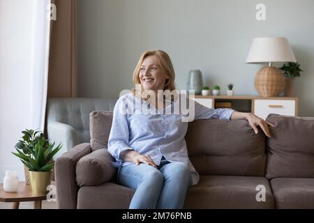 Gaie et attrayante jeune femme de retraite assise sur un canapé maison Banque D'Images