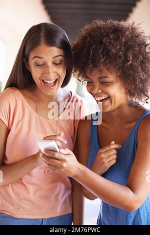Tous les sourires quand des amis traînent. deux copines se traînaient ensemble à l'aide d'un téléphone portable. Banque D'Images