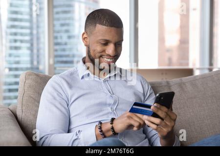 Un homme africain tenant une carte et un smartphone, dépensez de l'argent sur Internet Banque D'Images