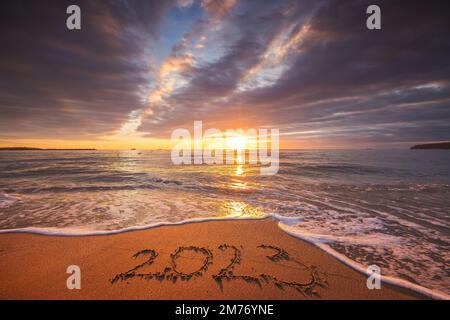 Concept du nouvel an 2023 heureux, lettrage sur la plage. Texte écrit sur la plage au lever du soleil. Banque D'Images