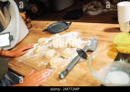 Disposition d'un morceau de pâte brute de forme ronde sur un comptoir en bois. Couper la pâte en morceaux à l'aide d'un couteau. Dessert maison. Banque D'Images