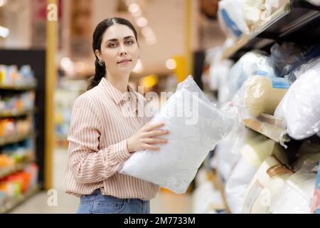 Portrait de caucasien jeune jolie femme portant des lunettes tient l'oreiller. Textiles domestiques au supermarché. Concept commercial. Banque D'Images