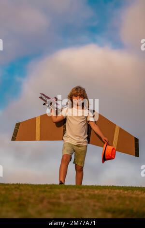 Enfance à la campagne. Enfant heureux jouant à l'extérieur. Enfant s'amusant avec des ailes de papier jouet. Banque D'Images