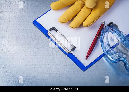 Lunettes en plastique gants de protection stylo bloc-notes sur fond métallique. Banque D'Images