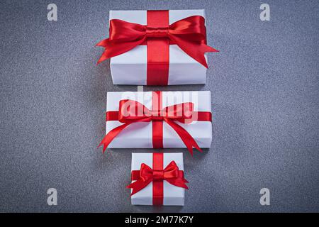 Boîtes-cadeaux blanches avec bandes rouges sur la surface grise concept de vacances. Banque D'Images