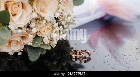 Une belle image aux tons avec des anneaux de mariage se trouve sur une surface noire sur le fond d'un bouquet de fleurs Banque D'Images