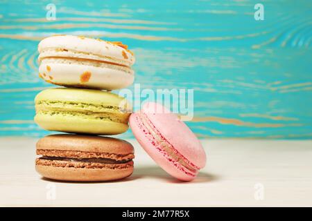 Macarons colorés, délicieuses pâtisseries françaises, empilées sur une table en bois blanc. Banque D'Images