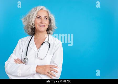 Femme mature médecin regardant vers le haut avec les bras croisés Banque D'Images