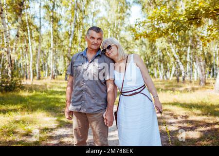 Portrait d'un couple de personnes âgées marchant à l'extérieur dans la forêt estivale. Les personnes âgées se tiennent les mains et s'embrasent. Banque D'Images