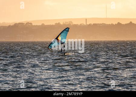 Planche à voile à Hill Head Hampshire Angleterre avec l'île de Wight et une brume orange du soleil se coucher en arrière-plan Banque D'Images