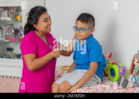 Une pédiatre souriante en vérifiant un enfant assis sur le lit de son bureau. Banque D'Images