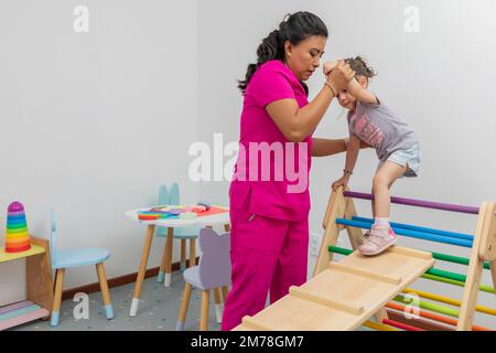 Fille monte le jeu en bois dans le bureau du médecin pédiatre, alors qu'ils l'aident à grimper. Banque D'Images