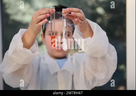 Détails: Tubes à essai avec des produits chimiques dans les mains d'un chimiste d'école, examinant les caractéristiques des substances à l'intérieur des tubes à essai Banque D'Images