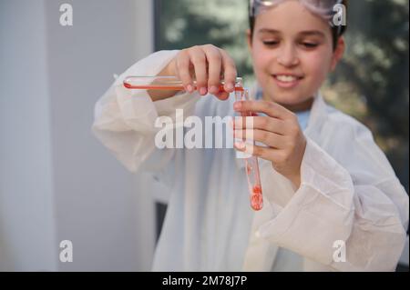 Détails: Mains d'un écolier flou versant un réactif dans une éprouvette pendant la classe de chimie dans un laboratoire d'école de sciences Banque D'Images