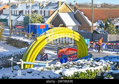 Un travailleur inspecte la neige glacée couverte de la route résidentielle du village les hommes arrêtent le travail sur l'infrastructure de remplacement du gaz principale conditions de travail dangereuses Angleterre Royaume-Uni Banque D'Images