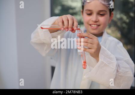 Détails: Mains d'un écolier flou versant un réactif dans une éprouvette pendant la classe de chimie dans un laboratoire d'école de sciences Banque D'Images